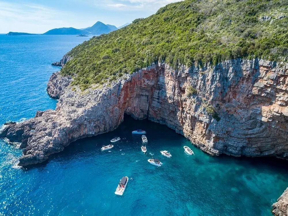 Boats gathered in front of the Blue Cave beneath the Luštica cliffs
