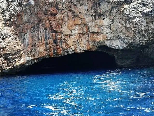 The dark mouth of the Blue Cave above glowing blue water